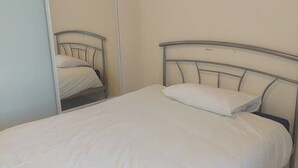 A single bed with a metal frame and white bedding in a room with a sliding door closet. - Grace House (Stockton-on-Tees)