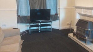 A living room with a flat-screen TV on a stand, a fireplace, and a sofa. - Grace House (Stockton-on-Tees)