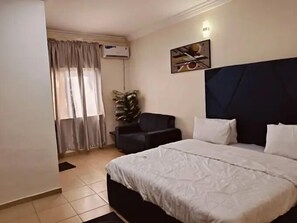 A hotel room with a large bed, a chair, a potted plant, and a painting on the wall.