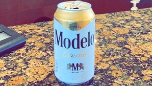 Una lata de cerveza Modelo sobre una encimera de granito, con el logotipo de Villa del Palmar Flamingos al fondo.
