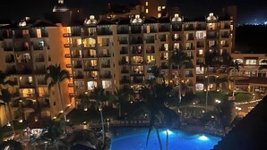 Un hotel de varios pisos con balcones, piscina y palmeras.