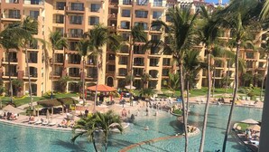 Un resort con una piscina grande, palmeras y un edificio de varios pisos con balcones.
