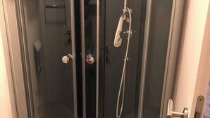 A glass-enclosed shower stall with a handheld showerhead and a wall-mounted faucet.
