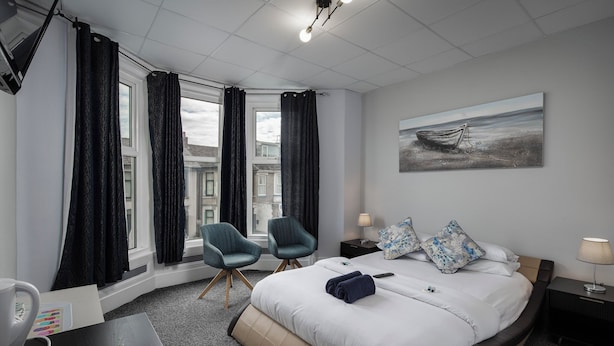 Une chambre d’hôtel avec un lit, deux chaises, un bureau, une lampe et un tableau au mur.