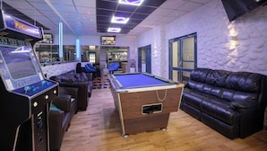 A pool table, two leather sofas, a bar area, and a billiards machine in a room with a patterned wall and a ceiling with geometric light fixtures. - 100 Pipers Hotel (Blackpool)