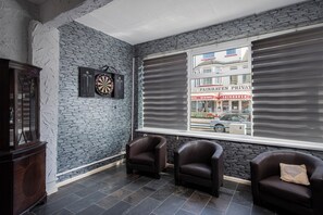 Ein Zimmer mit Stehwänden, einer Dartscheibe, zwei Ledersesseln, einem Schrank und einem Fenster mit Blick auf ein Gebäude.