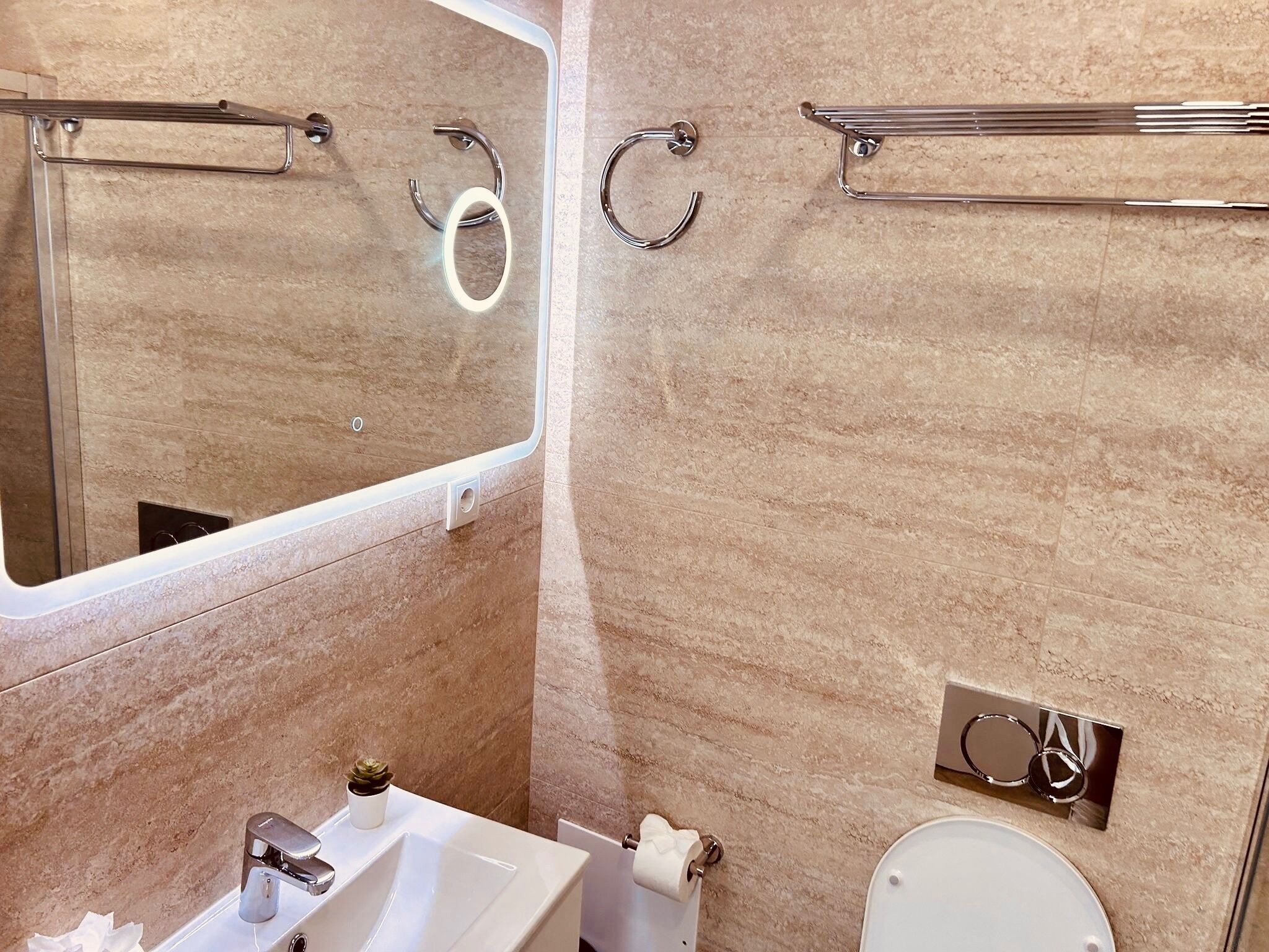 Une salle de bain équipée d’un lavabo, d’un miroir, de toilettes, d’un porte-serviettes et d’un distributeur de serviettes.