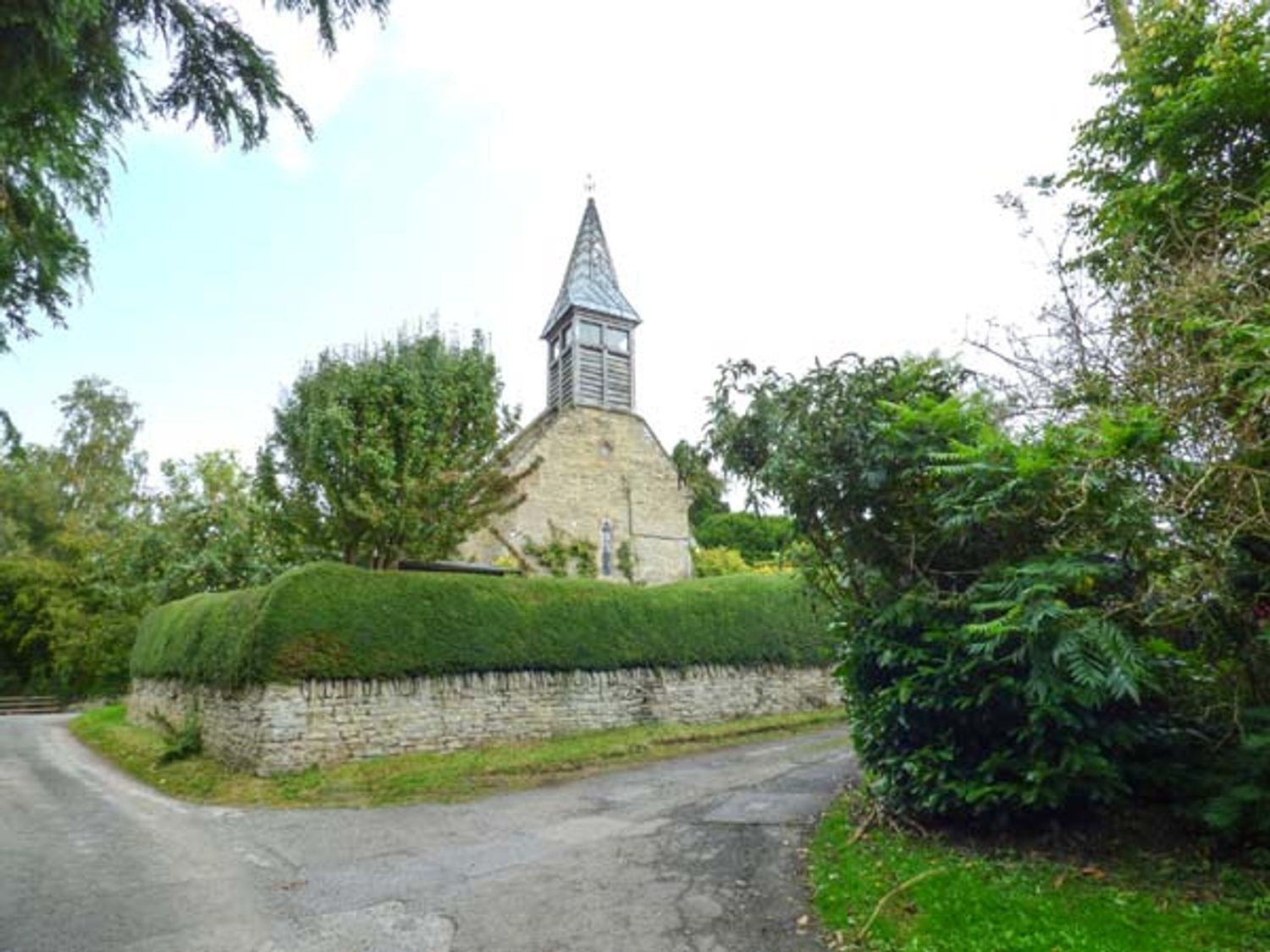 A stone church with a pointed steeple, surrounded by greenery and a stone wall.