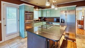 Una cocina con gabinetes color turquesa, electrodomésticos de acero inoxidable y una isla con encimera de granito.
