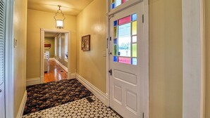 Un pasillo con alfombra estampada, una puerta blanca con paneles de vidrio de colores y una lámpara sobre ella.