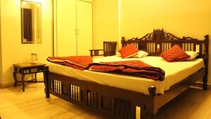 A bedroom with a wooden bed, a nightstand, a wardrobe, and a mirror. - Hotel Chit Chat Palace (Jaipur)