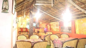 A restaurant with wicker chairs and tables, a thatched roof, and hanging lanterns. - Hotel Chit Chat Palace (Jaipur)