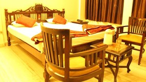A hotel room with a large bed, two wooden chairs, a small table, and a curtain. - Hotel Chit Chat Palace (Jaipur)