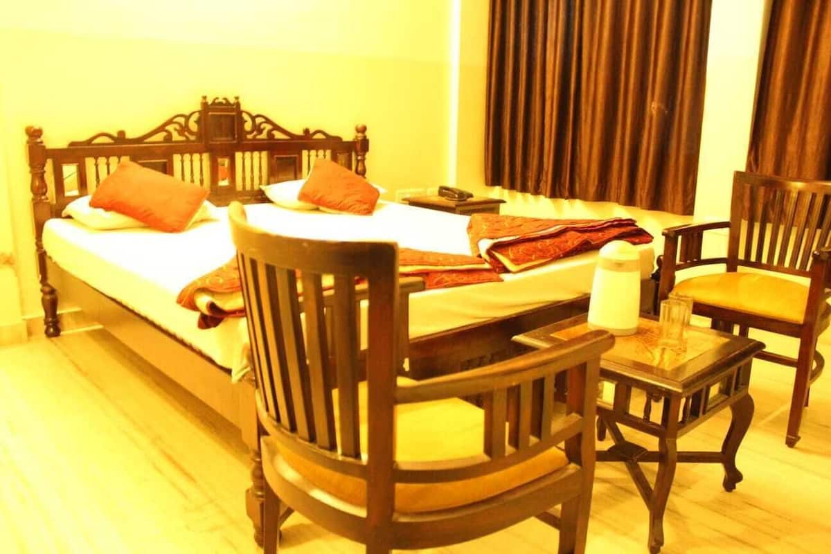 A hotel room with a large bed, two wooden chairs, a small table, and a curtain.
