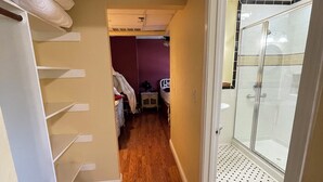 A narrow hallway with wooden flooring, a bed with a white headboard, and a glass shower enclosure.