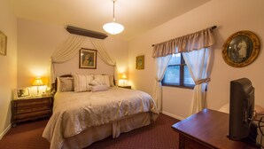 A hotel room with a large bed, bedside lamps, a wooden nightstand, a television on a wooden table, and a window with curtains. - Boutique Retreat in Wine & Gold Country (Placerville)