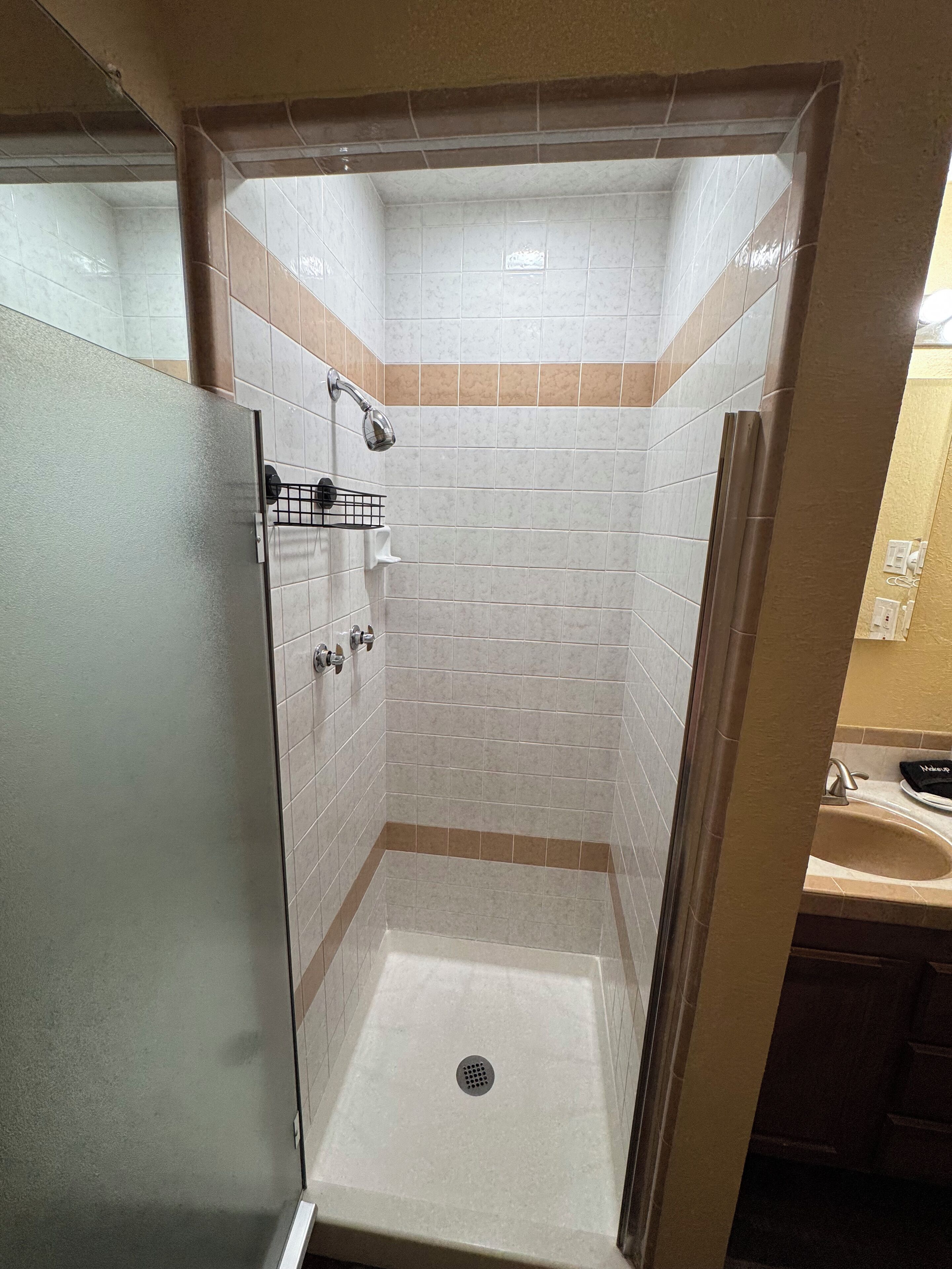 A small, enclosed shower stall with a glass door, tiled walls, and a drain in the center.