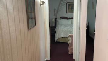 A narrow hallway with a patterned carpet, a bed with a canopy in the background, and a mirror on the right wall.