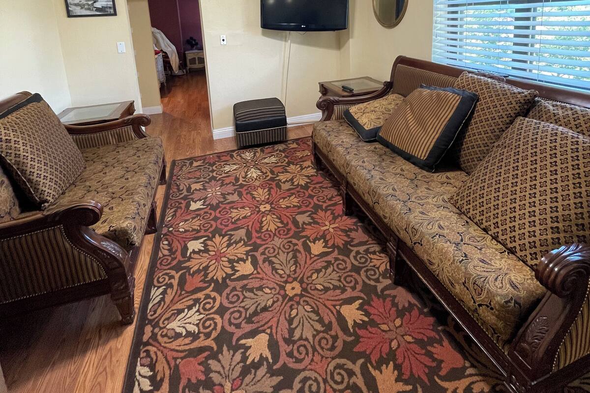 A living room with a ceiling fan, a television mounted on the wall, a patterned sofa, and a wooden floor.