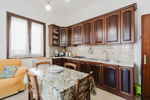 Une cuisine compacte avec des meubles en bois, une table à manger avec des chaises, un four encastré et une fenêtre avec des stores.