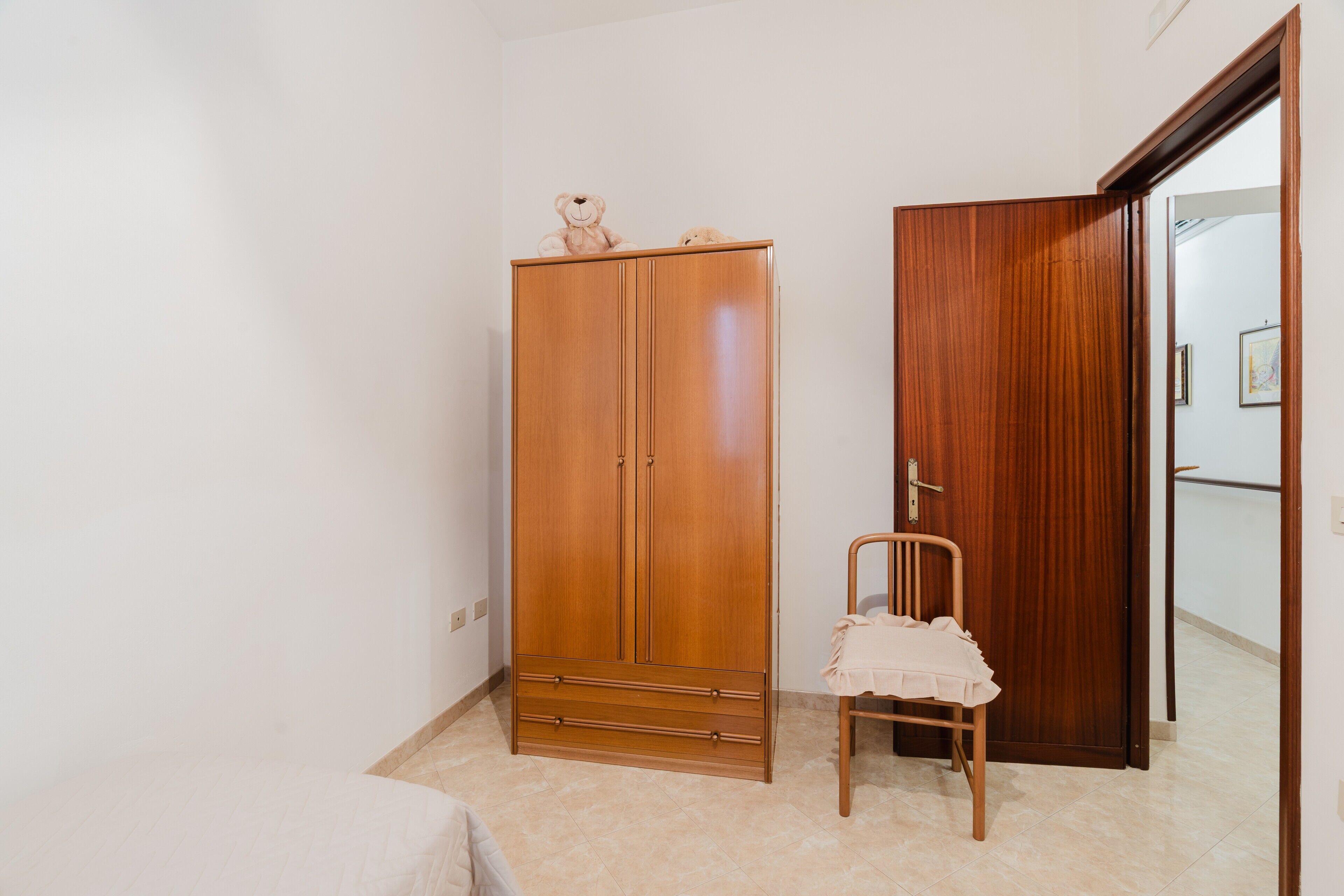 Une pièce avec une armoire en bois, une chaise et une porte donnant sur une autre pièce.