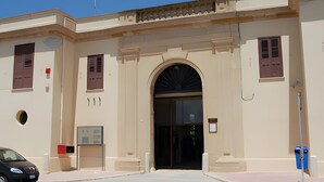 A building with a large arched entrance, a flagpole, and a car parked in front. - Holiday Home 'La Piazzetta' with Wi-Fi and Air Conditioning (Marsala)