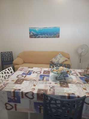 A dining area with a table covered in a nautical-themed tablecloth, a sofa, and a wall-mounted picture of an underwater scene.