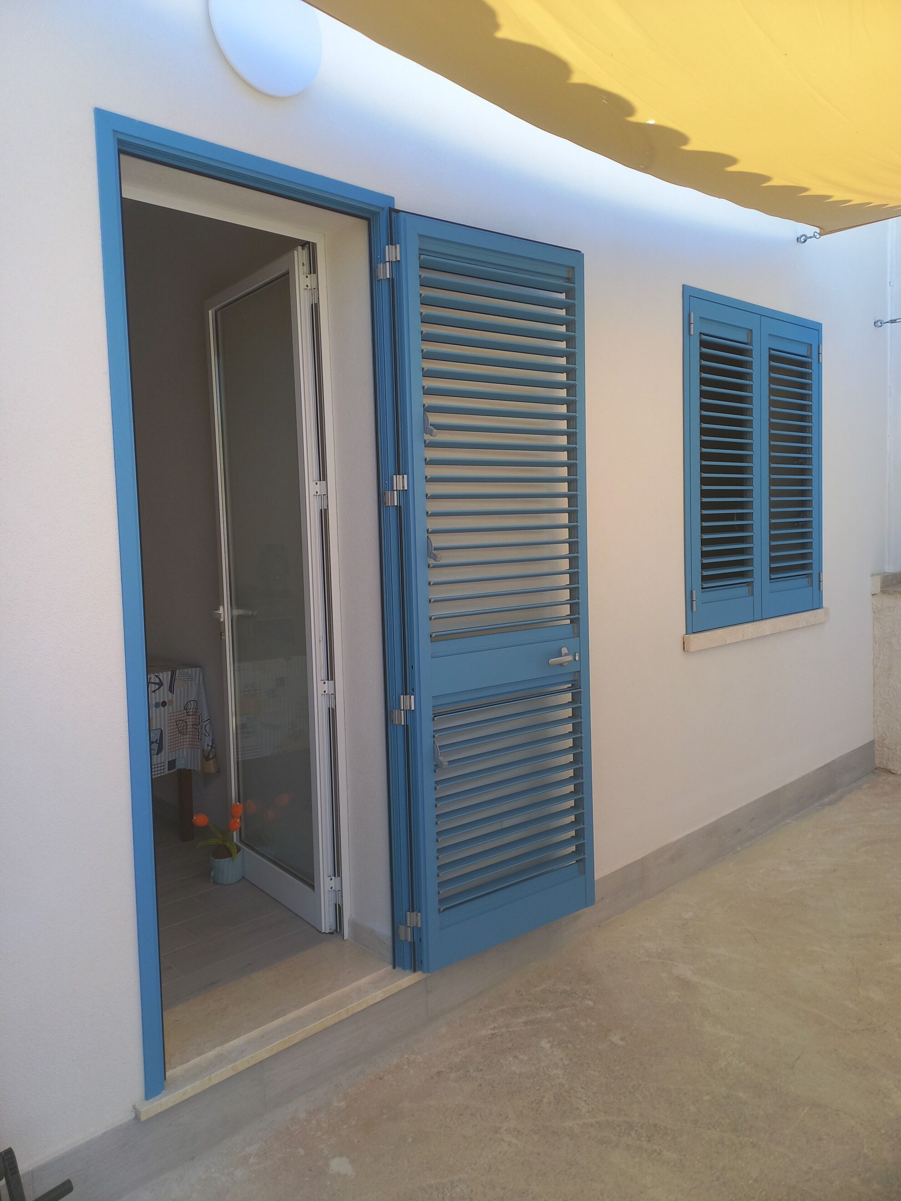 A room with a sliding door, a window with shutters, and a small table with a chair.
