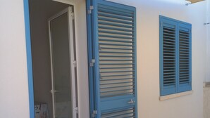 A room with a sliding door, a window with shutters, and a small table with a chair. - Holiday Home 'Casa Damari-Beachfront' with Sea View and Private Terrace (Petrosino)