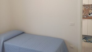 A single bed with a blue bedspread in a room with a wooden floor and a white door leading to a bathroom with a tiled backsplash. - Holiday Home 'Casa Damari-Beachfront' with Sea View and Private Terrace (Petrosino)
