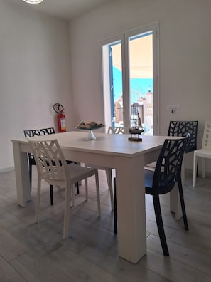 A dining area with a table and chairs, a fire extinguisher, and a view through a door.