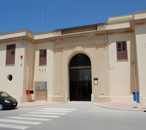 A building with a large arched entrance, a flagpole, and a car parked in front.