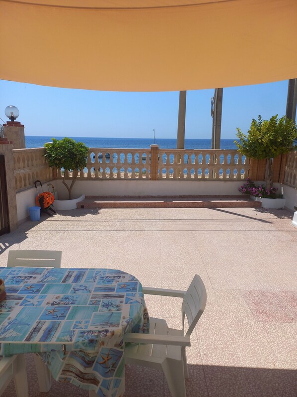 An outdoor patio with a table and chairs, a view of the sea, and a decorative fence.
