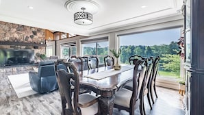 A spacious dining area with a large table and chairs, a stone fireplace, and a view of a forest. - 5-Bedroom Countryside Estate in Northern GTA – Ideal for Gatherings & Getaways (Bolton)