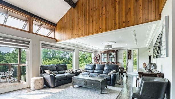 A spacious living room with a large sectional sofa, a coffee table, and a fireplace. There is a dining area with a wooden table and chairs. The room has large windows offering a view of the outdoors. - 5-Bedroom Countryside Estate in Northern GTA – Ideal for Gatherings & Getaways (Bolton)