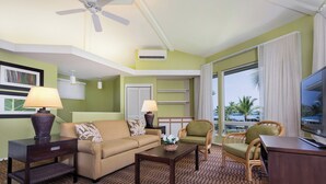 Habitación de hotel con sofá, sillón, mesa de centro y televisor. Cuenta con ventilador de techo, aire acondicionado y ventana con cortinas.