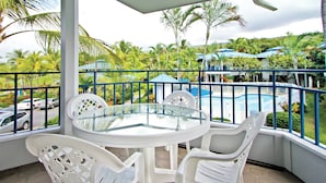 A covered outdoor seating area with a glass table and white plastic chairs, overlooking a pool and lush greenery. - Stay in paradise minutes from the beach (Kailua Kona, Island of Hawaii)