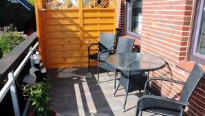 A patio with a round table and four chairs, a potted plant, and a wooden fence.