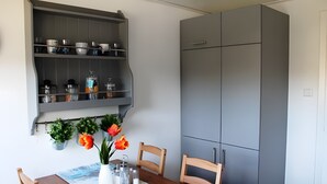 A dining area with a table, chairs, a grey cabinet, and a wall-mounted shelf with dishes and potted plants.