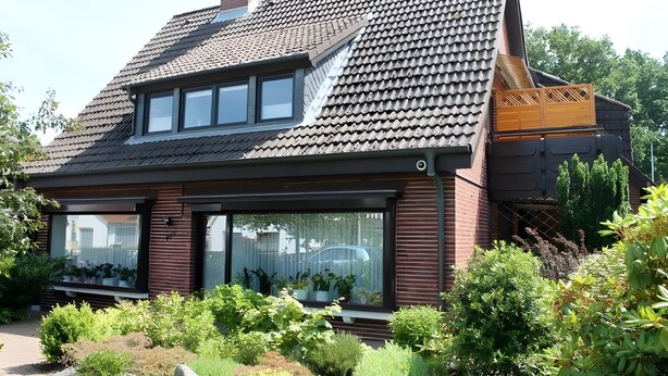 A modern house with a sloped roof, large windows, and a garden.