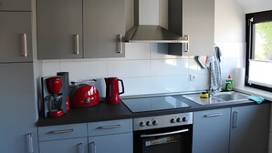 A modern kitchen with grey cabinets, a stainless steel range hood, a red coffee maker, a sink, and a window with a view of greenery.
