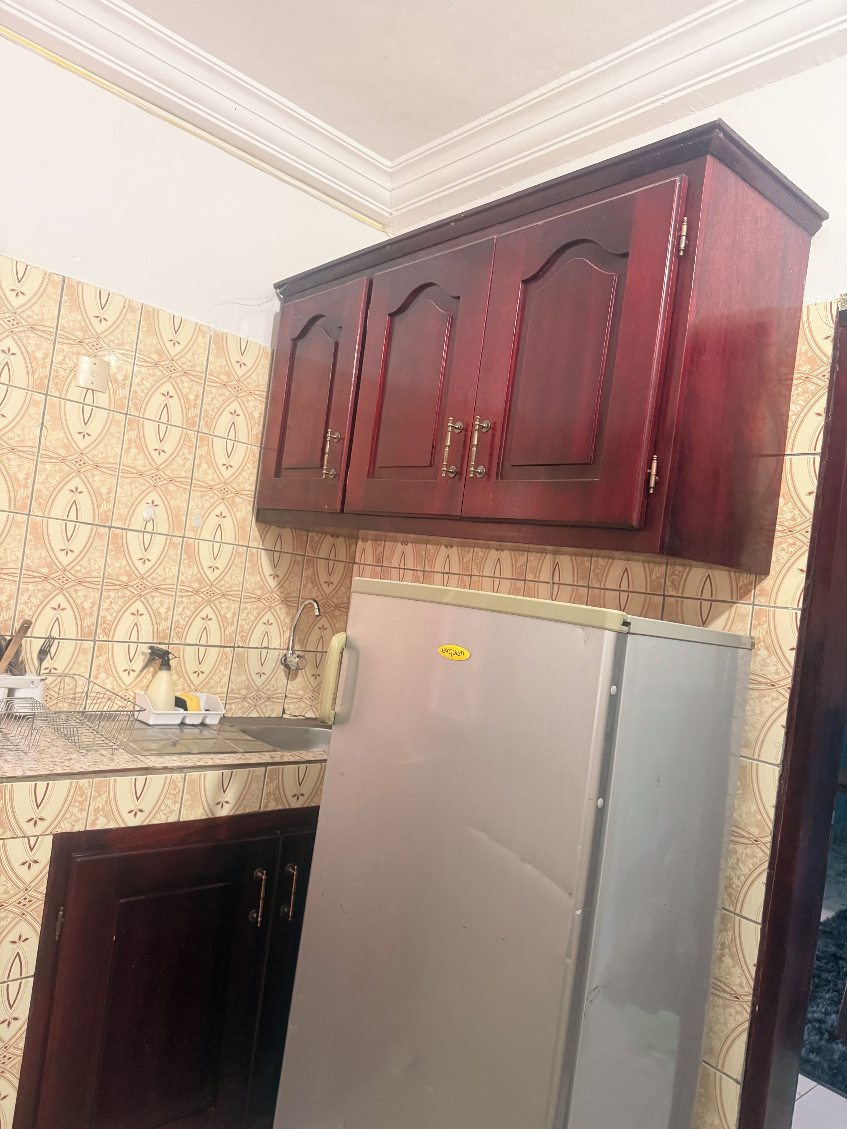 A kitchen with patterned tiles, a stainless steel refrigerator, and wooden cabinets.