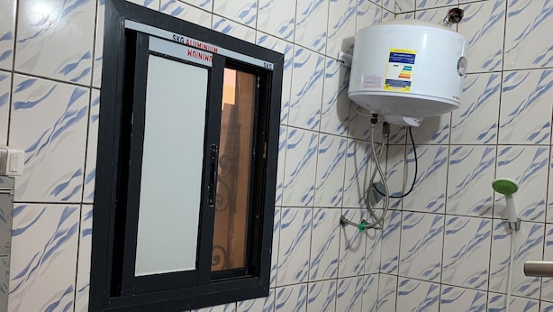 A bathroom with a white and blue marble tile pattern, a water heater mounted on the wall, a showerhead, and a handrail.