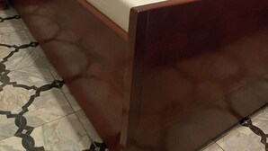 Ein Bett mit weißer Bettwäsche und einem gelben Handtuch, ein Holz-Kopfteil und ein Fliesenboden mit geometrischem Muster.