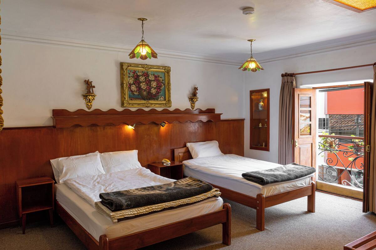 A hotel room with two wooden beds, a nightstand, a painting, and a balcony with a railing.