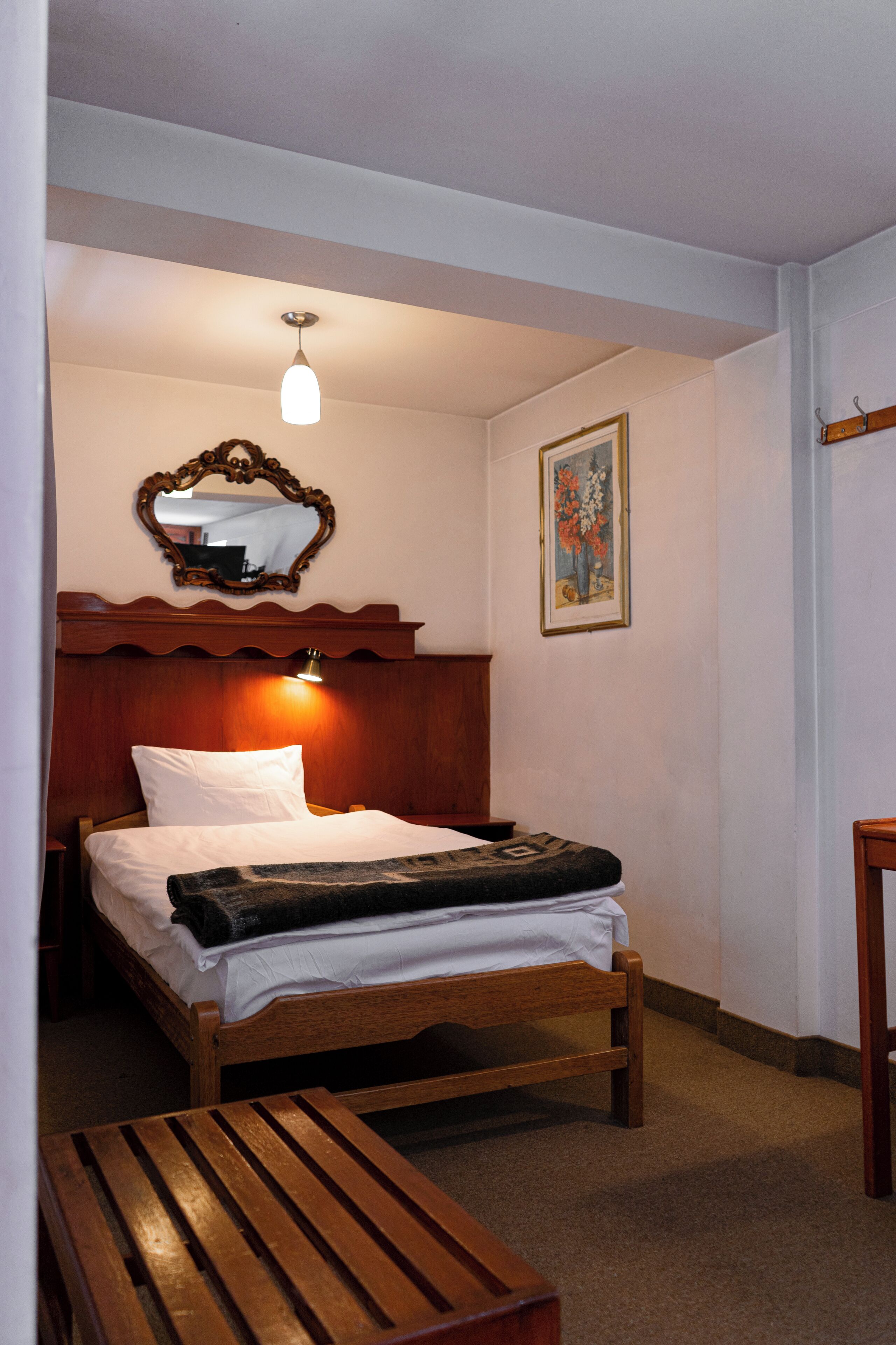 Una cama bien hecha con cabecera de madera, una lámpara de noche y un cuadro en la pared.