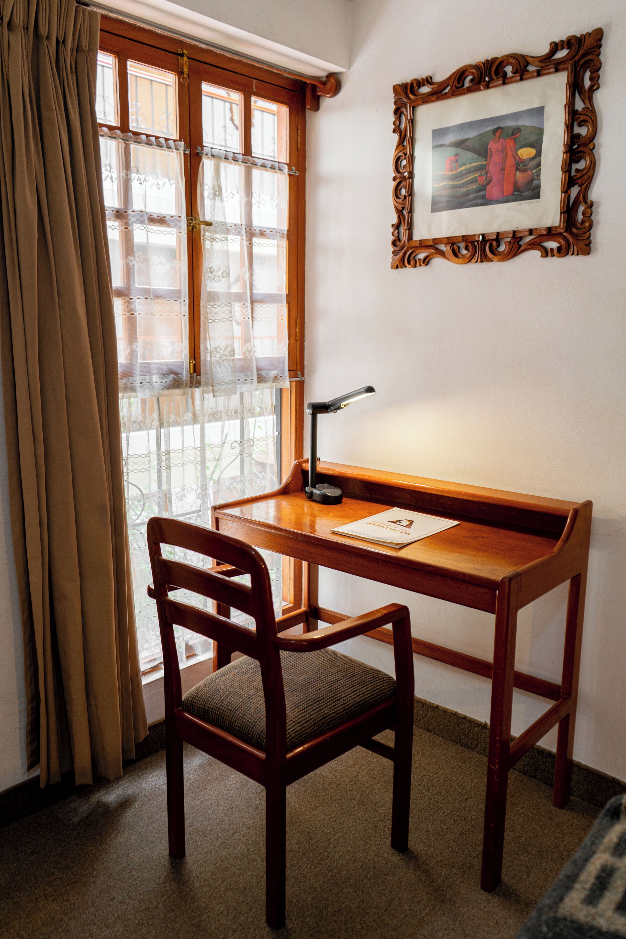 Un escritorio de madera con una silla, una lámpara y un cuadro en la pared.