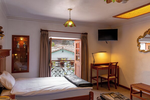 A hotel room with a bed, a desk, a chair, a TV, a mirror, and a window with curtains. - La Posada de Atahualpa (Cusco)