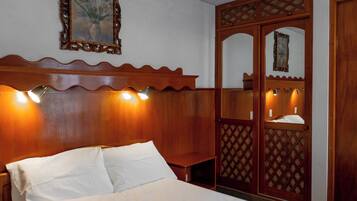 Habitación de hotel con cabecera de madera, cama con ropa de cama blanca y un espejo decorativo con luces.