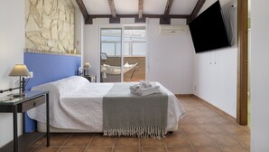 A bedroom with a bed, a desk, a chair, a TV, and a stone wall. - Apartment 'Las Niñas' with Private Terrace, Wi-Fi and Air Conditioning (Olvera)